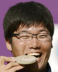 アーチェリー男子個人で獲得した銀メダルをかじる笑顔の古川高晴（共同）