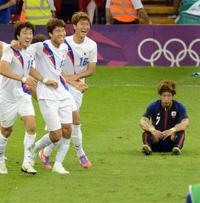 喜ぶ韓国選手らを前にぼうぜんとピッチに座り込む大津（右）（撮影・菅敏）